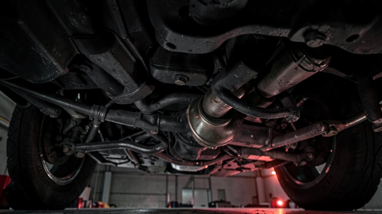 Underside of a vehicle on a lift showing gearbox, driveshafts and exhaust during a drivetrain inspection